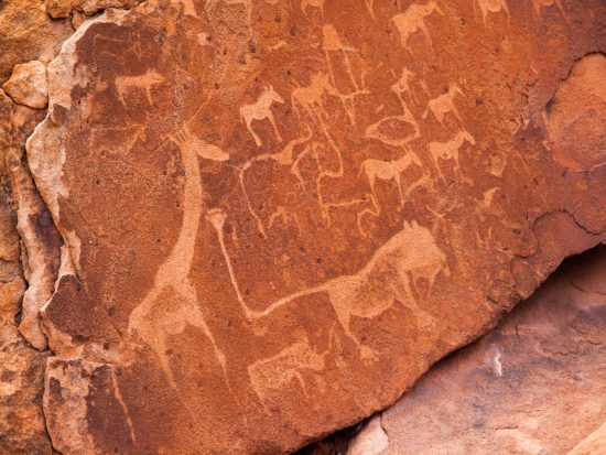 Felsmalereien der San auf braunem Stein: Giraffe, Löwen und weitere wilde Tiere