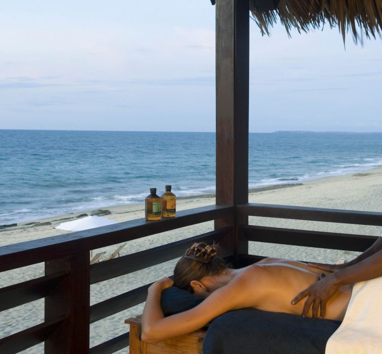 „digitale Detox“-madagascar-rhino-africa-travel-remote-places Eine Frau bekommt eine Massage auf einer Terrasse, daneben das Meer und Strand