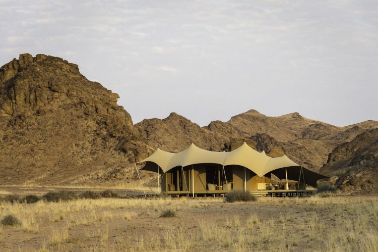 "digitale detox"-rhino-africa-travel-hoanib-skeleton-coast-camp-room-twin-bed-tent-family-tent-exterior-1 Ein Camp in der Wüste, dahinter eine Bergkulisse