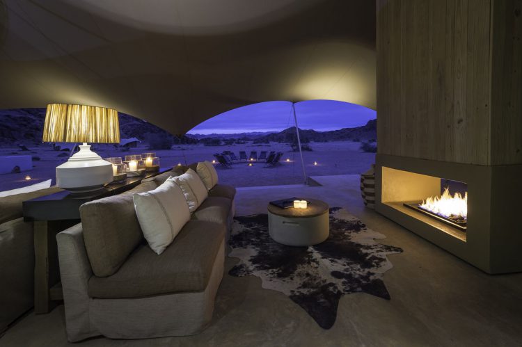"digitale detox"-rhino-africa-travel-hoanib-skeleton-coast-camp-room-twin-bed-tent-family-tent-lounge-5 Eine Couch vor einem offenen Kamin, dahinter Wüste in der Nacht