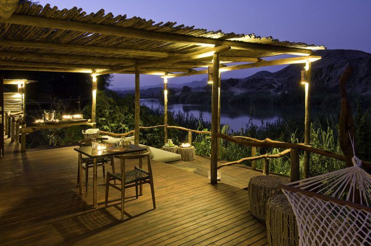 „digitale Detox“-rhino-africa-namibia Holzterrasse mit einem kleinen Tisch und zwei Sesseln, daneben ein Gewässer