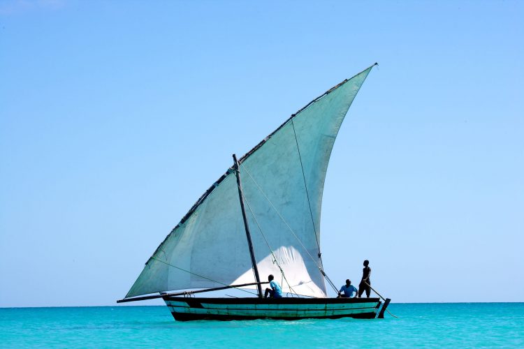 digitales-detox-rhino-africa-travel-vamizi-island-land-cruise-remote-places-mosambik Ein Segelboot mit drei Personen im Wasser, dahinter blauer Himmel