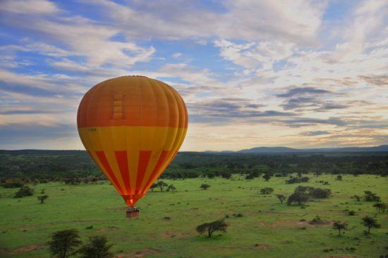 Ein gelb-orangener Heißluftballoon fliegt über den Krüger Nationalpark