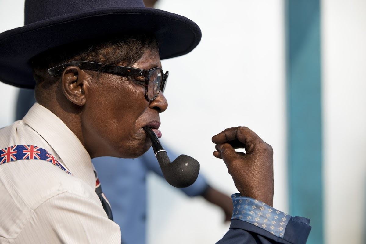 A Sapeur in Brazzaville wearing a top hat and smoking a pipe