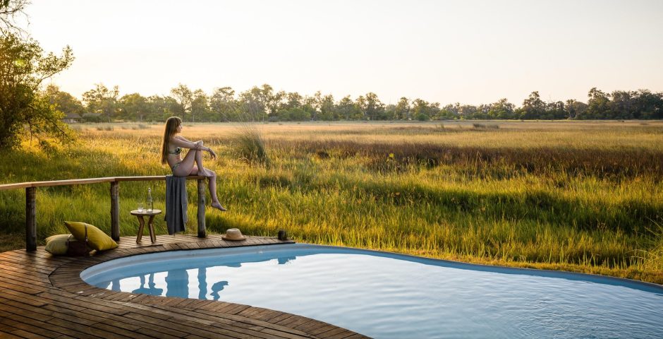 A woman sits beside a private pool overlooking the open wilderness, embodying the calm and freedom of a return trip to Africa.
