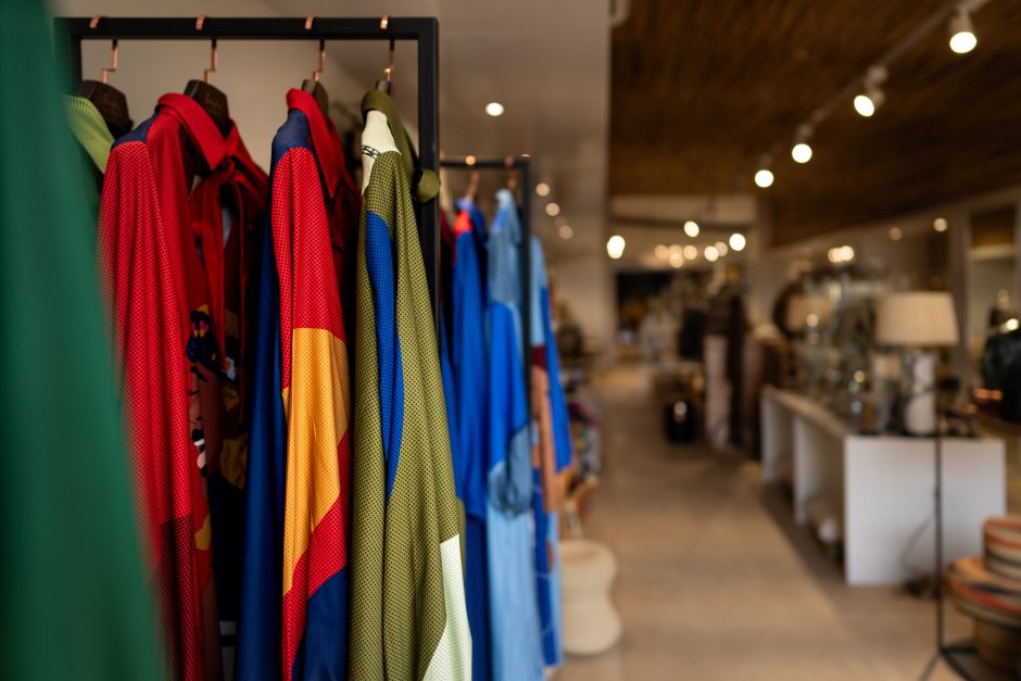 Singita Kruger National Park_Boutique and Gallery_Thebe Magugu Garments A colorful rack of garments is displayed in the boutique safari shop at Singita Kruger National Park, with the gallery's modern interior softly blurred in the background.