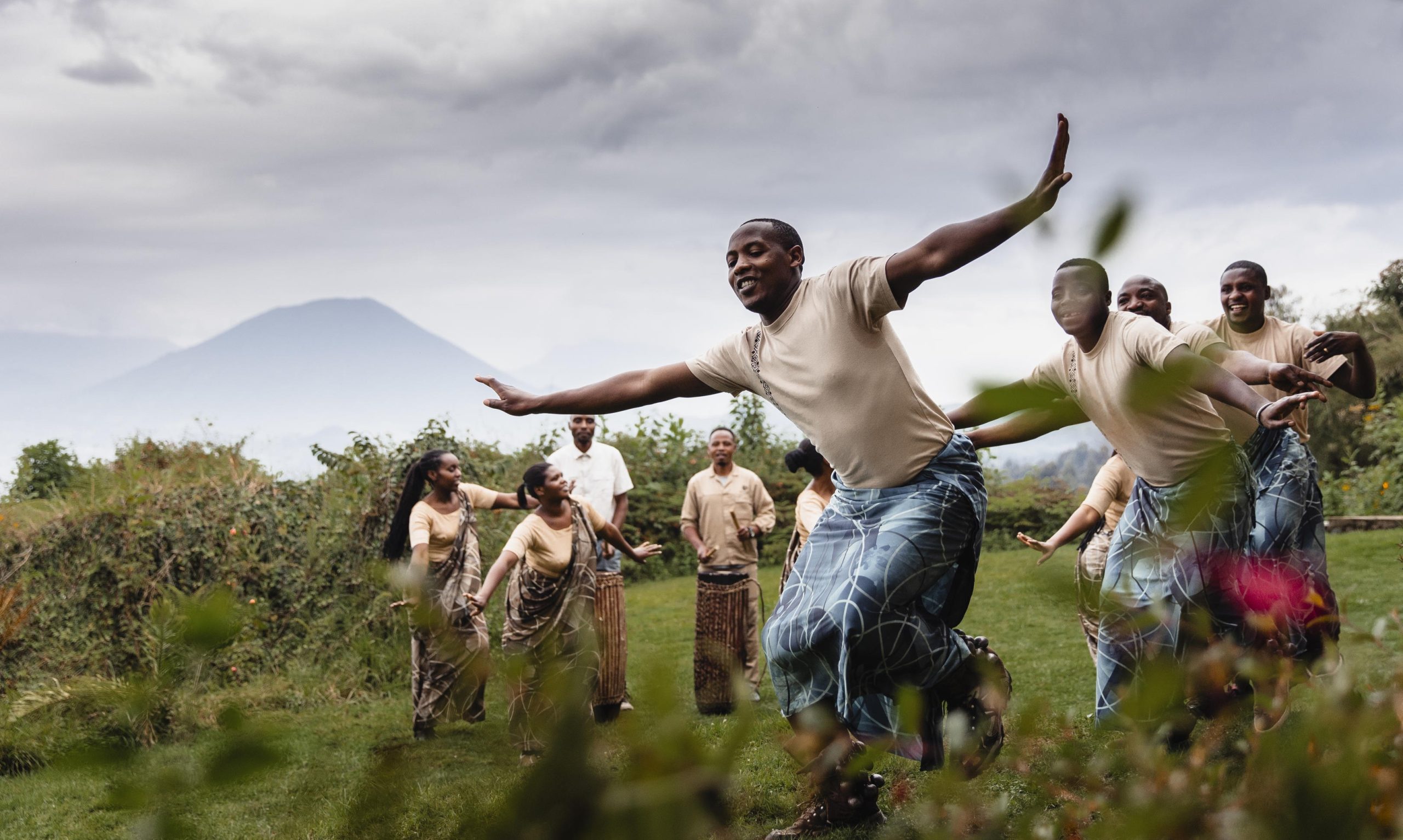 Wilderness-Sabyinyo-cover A group of Rwandan dancers perform joyfully outdoors with mountains in the distance, their movements full of energy and pride.