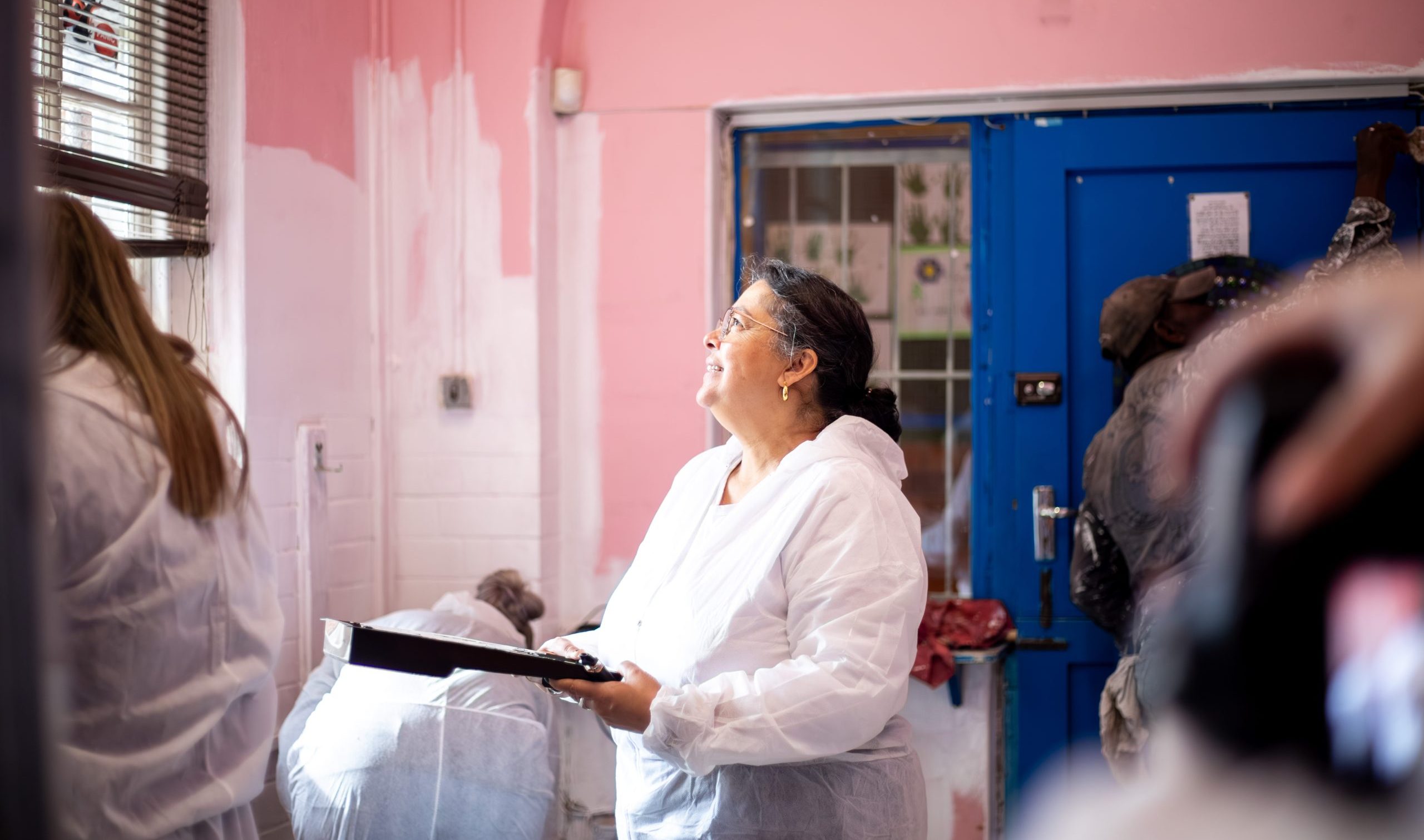 A Rhino Africa volunteer in a white suit smiles while painting a classroom wall