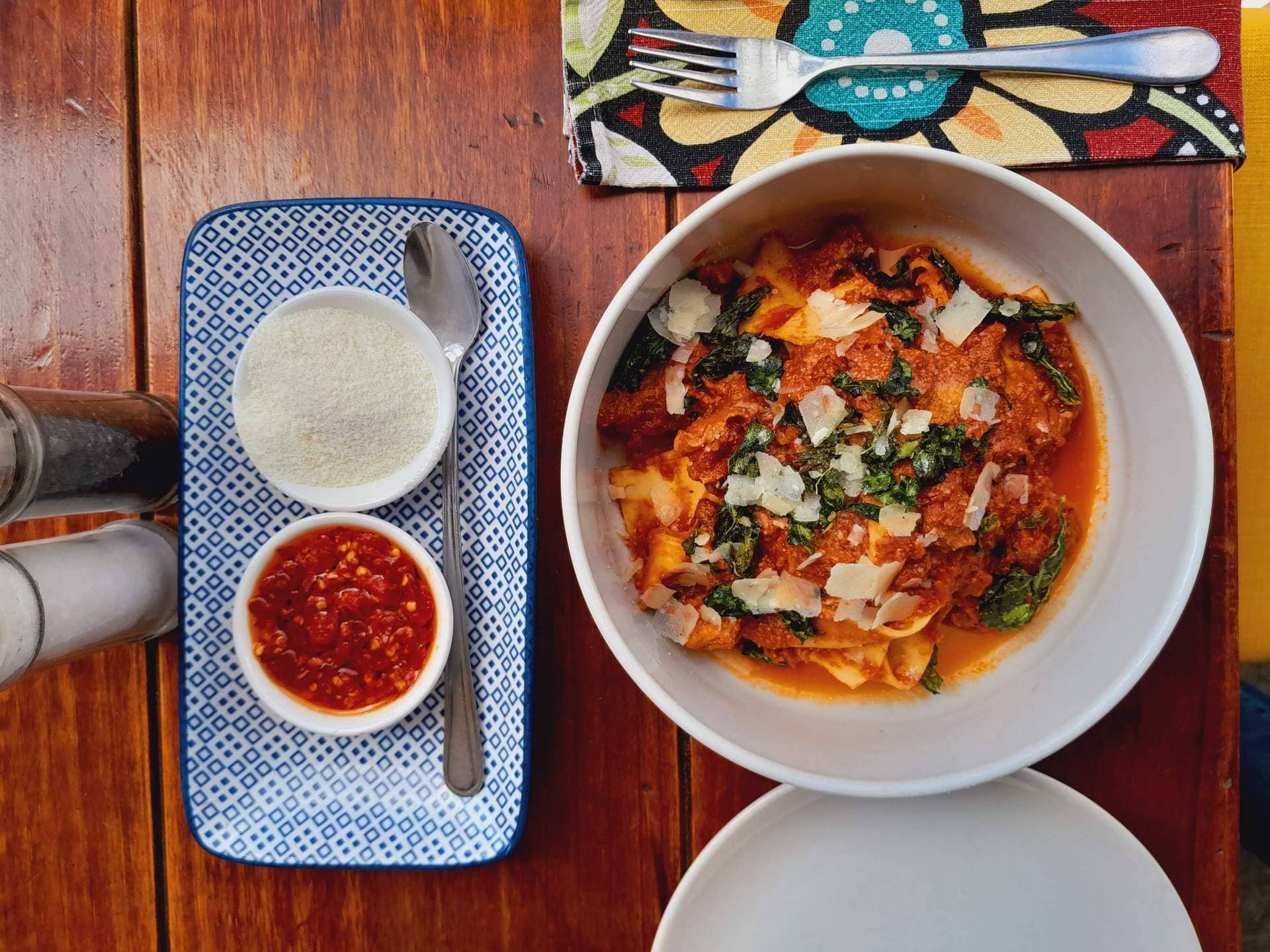 20230509_114719 A bowl of Italian pasta with a chili sauce and parmesan cheese on the side.