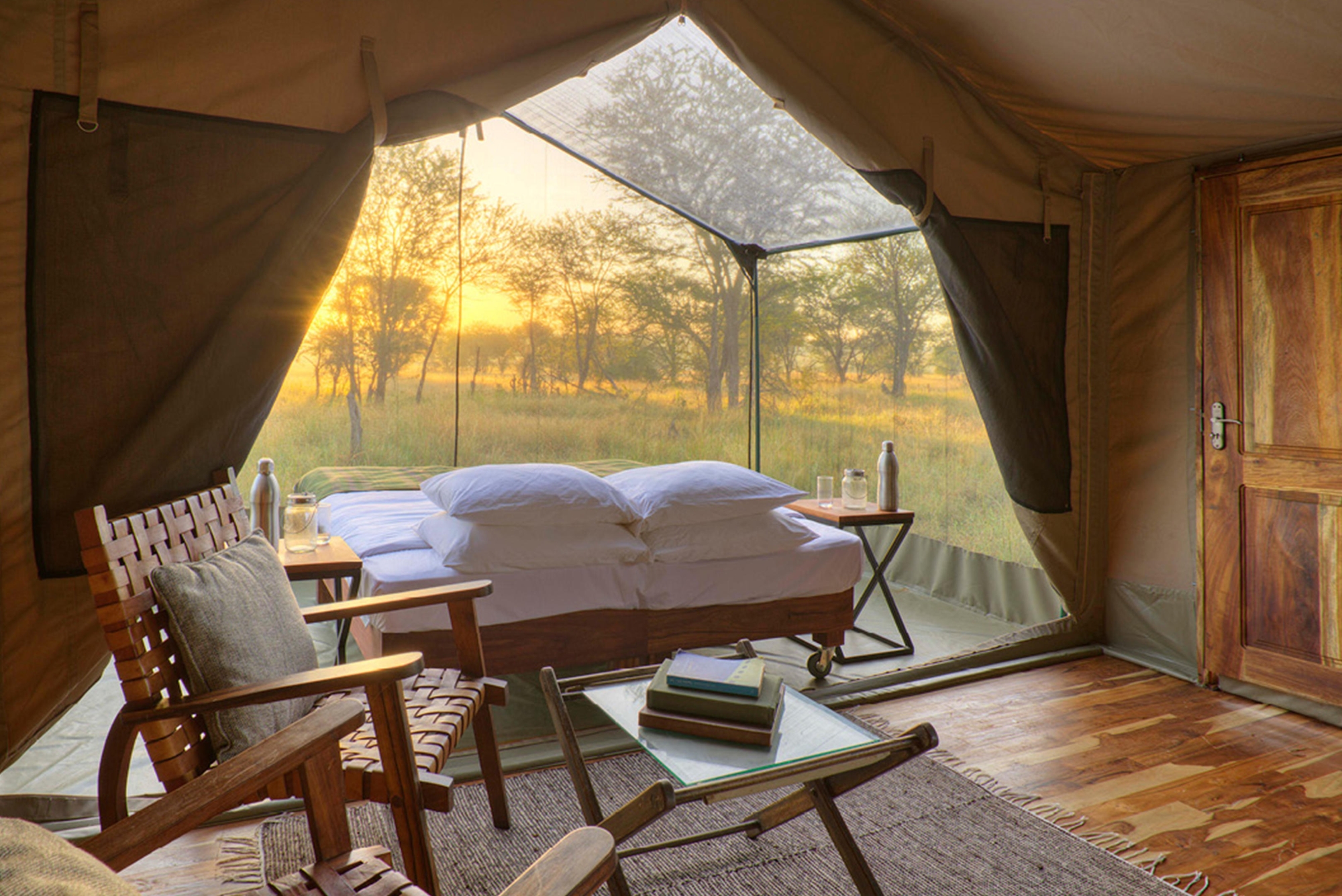 Asilia’s-Olakira-Migration-Camp-view-from-lounge-area Sunlight spills through mesh panels onto a made-up bed inside one of Tanzania’s mobile tented camps, surrounded by natural textures and thoughtful details.