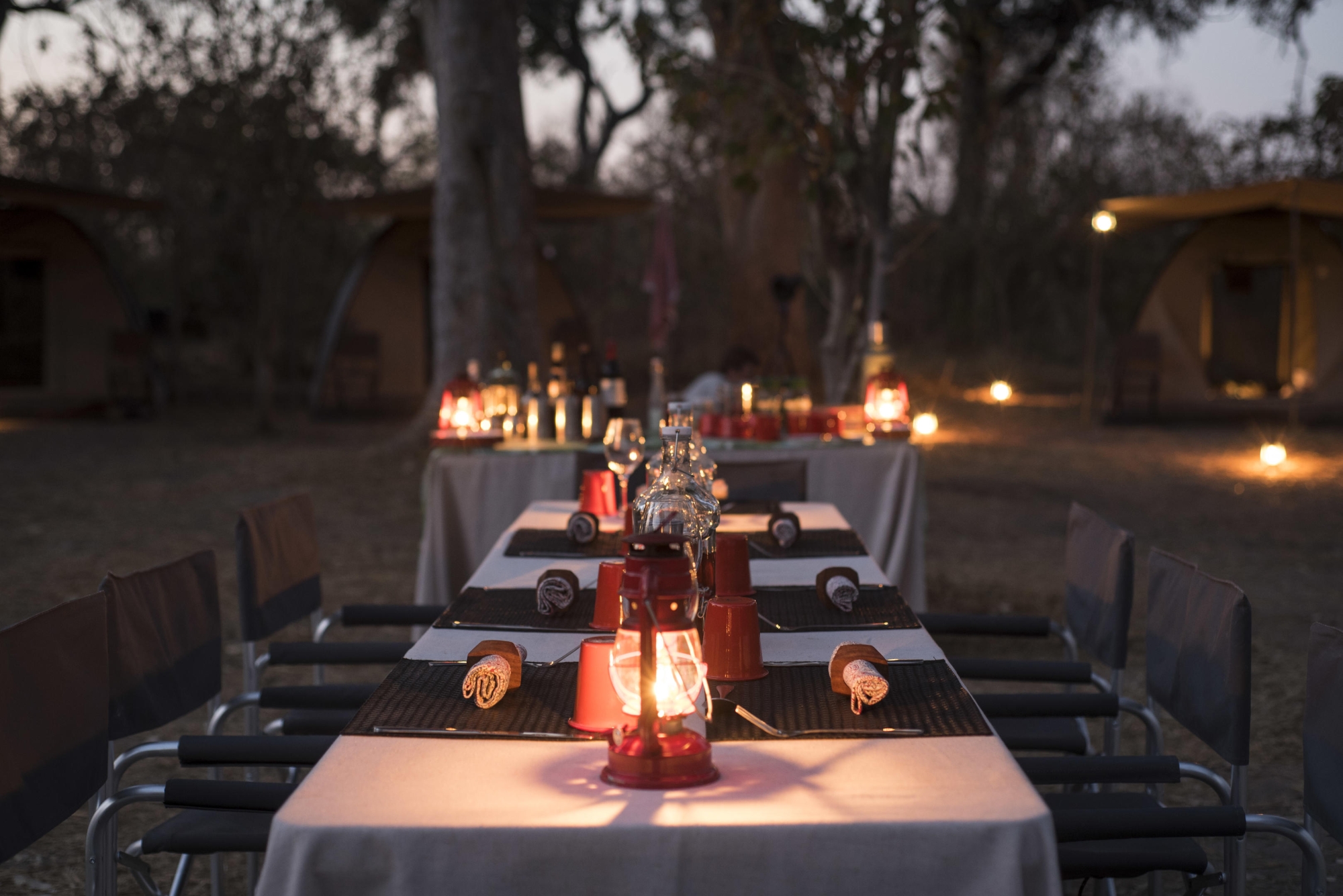 Beagle-Expeditions-Kweene-Trails-Botswana-dining A candlelit dining setup with lanterns and canvas tents forms part of a mobile tented camp in Botswana, ready for guests to gather under the stars.
