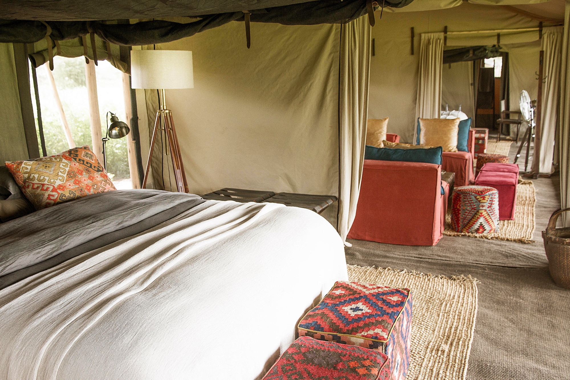 Legendary-Nyasi-Tented-Camp-tent-interior A spacious interior of one of Tanzania’s mobile tented camps features a king-sized bed, woven rugs, and colourful lounge seating beneath canvas walls.