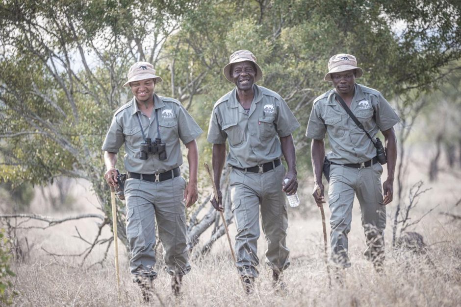 Three smiling Rhino Guardians walking together through bushveld as part of their training.