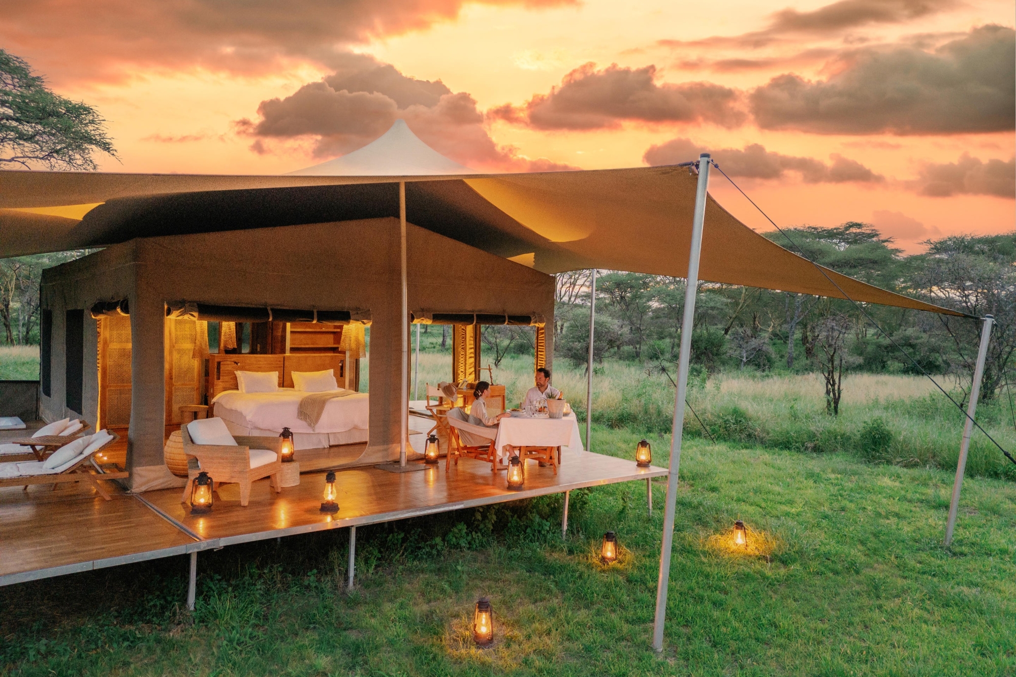 Roving-Bushtops-romantic-dinner A couple dines on the deck of one of Africa’s most luxurious mobile tented camps, framed by lantern light and a glowing Serengeti sunset.