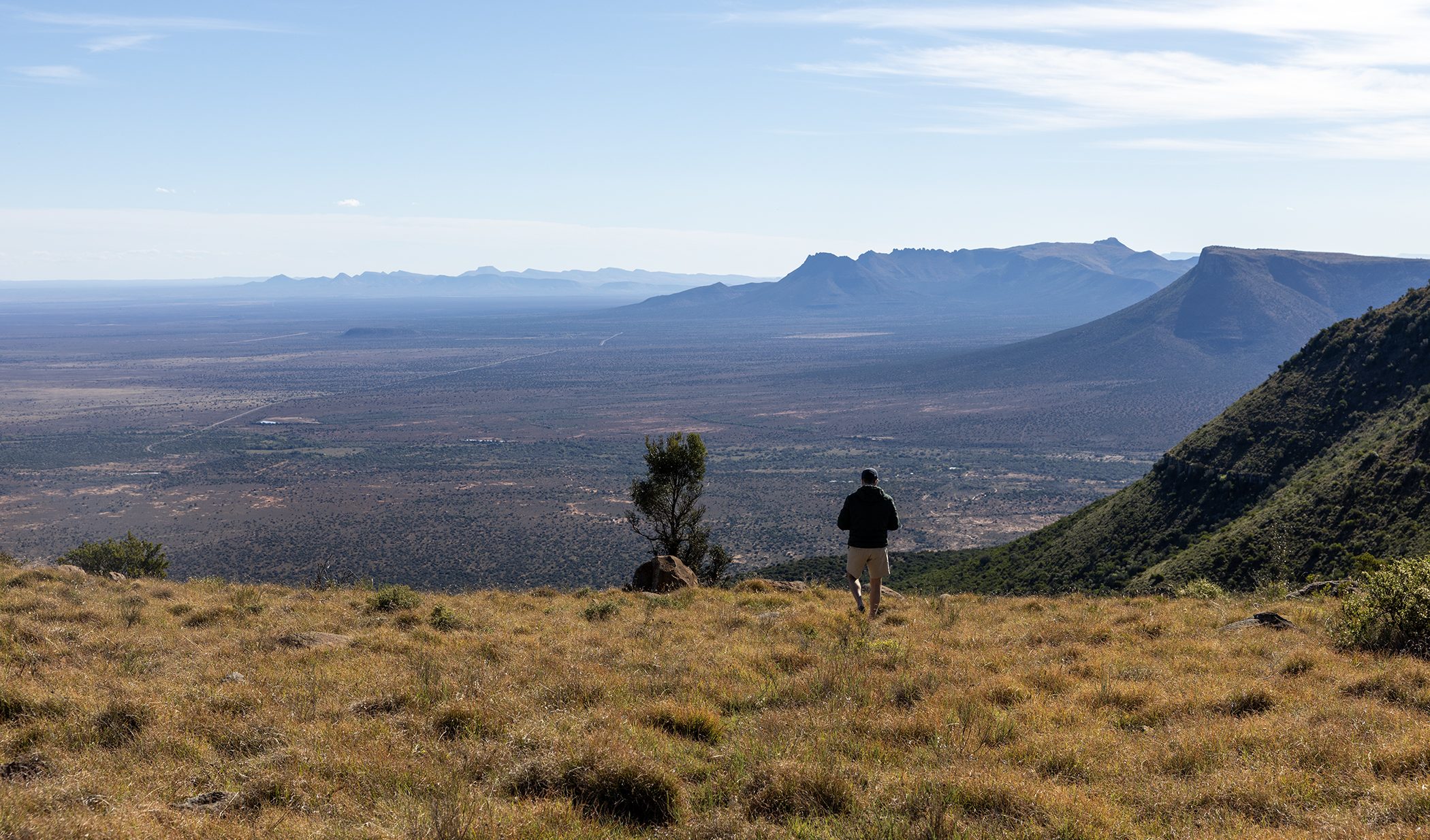 A man looks out over the vast Karoo plains and mountain ranges from a high vantage point.