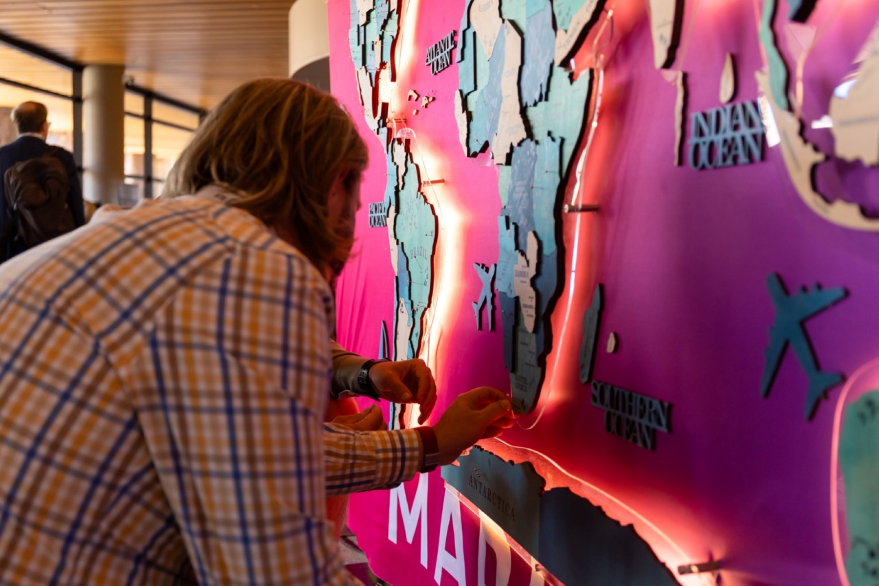 A person pins a marker onto a brightly lit world map display featuring Africa and surrounding continents.