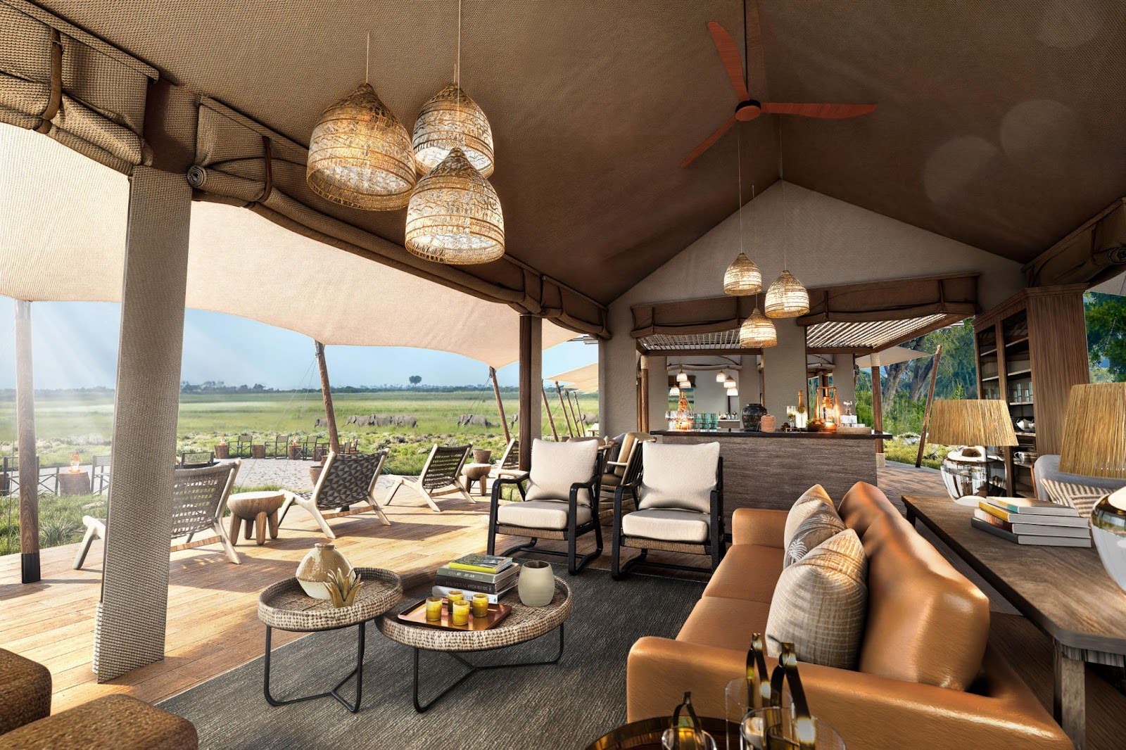 A spacious open-sided safari tented lounge that is well furnished and has a view of elephants walking nearby