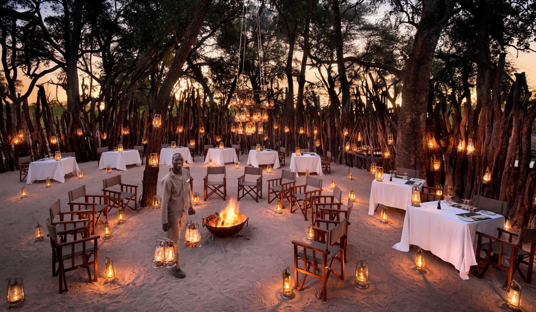 Lanterns glow around a firelit boma where a guide prepares the space for an evening that feels like a living manifesto of connection.