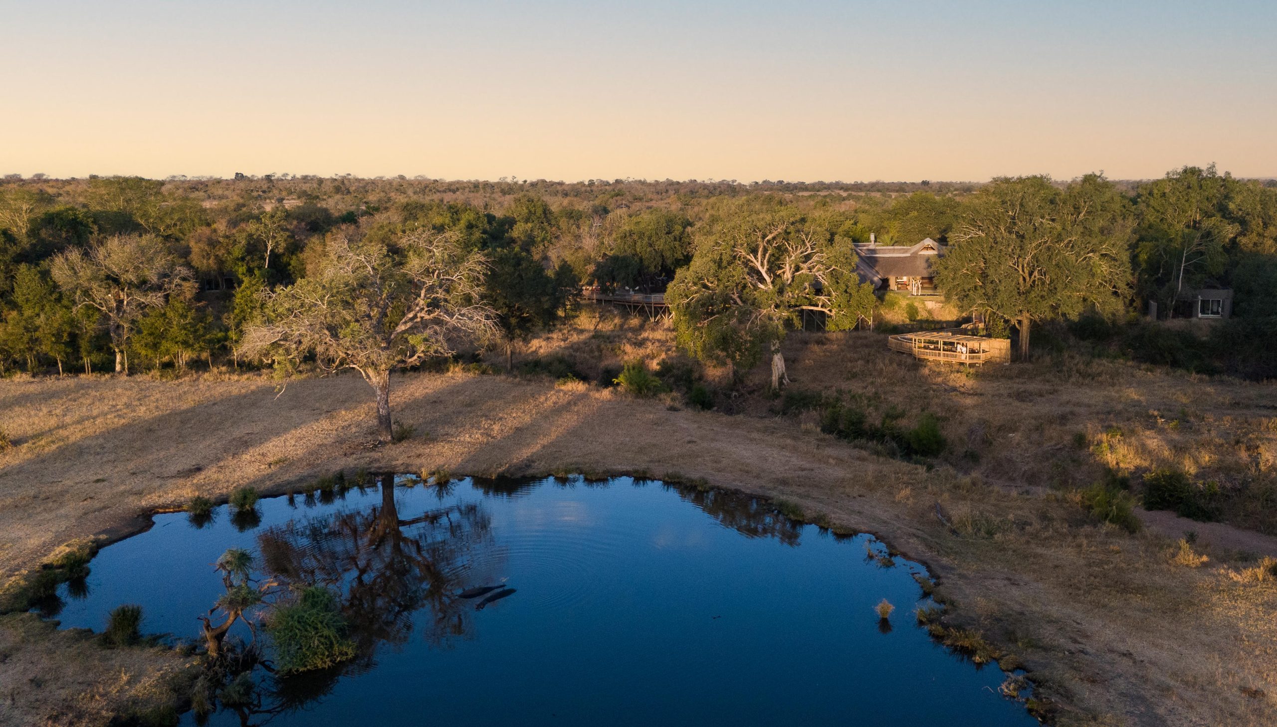 An aerial view shows a secluded safari lodge overlooking a quiet, reflective waterhole surrounded by bushveld, capturing the stillness offered by lodges with the best waterholes.