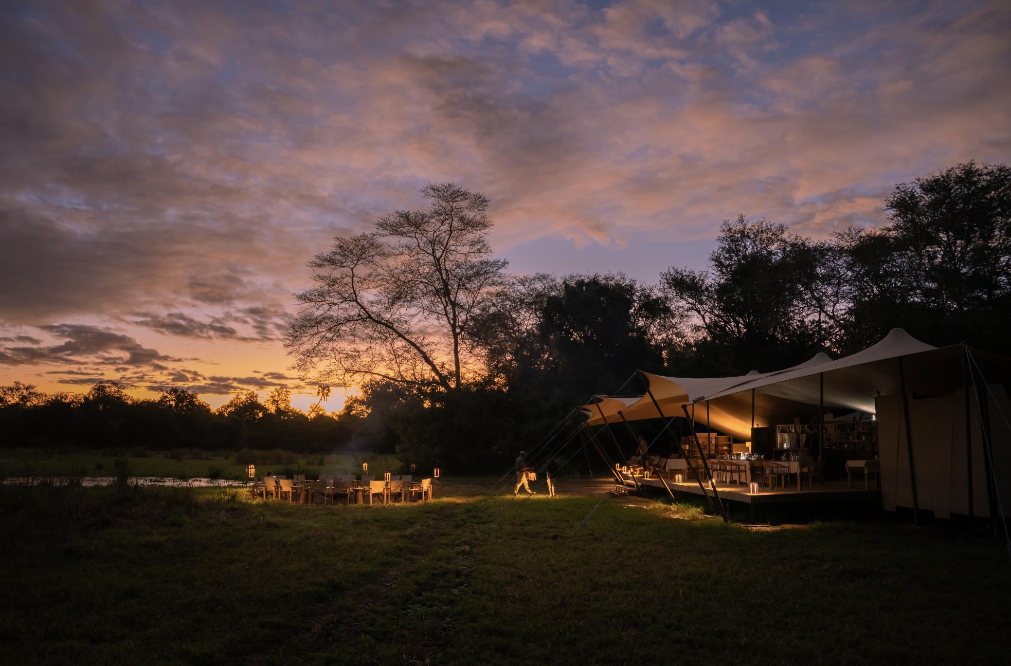 Main Area at night A softly lit safari camp glows beneath a dramatic sunset sky, showing how thoughtful tourism supports conservation through the impact in Gorongosa.