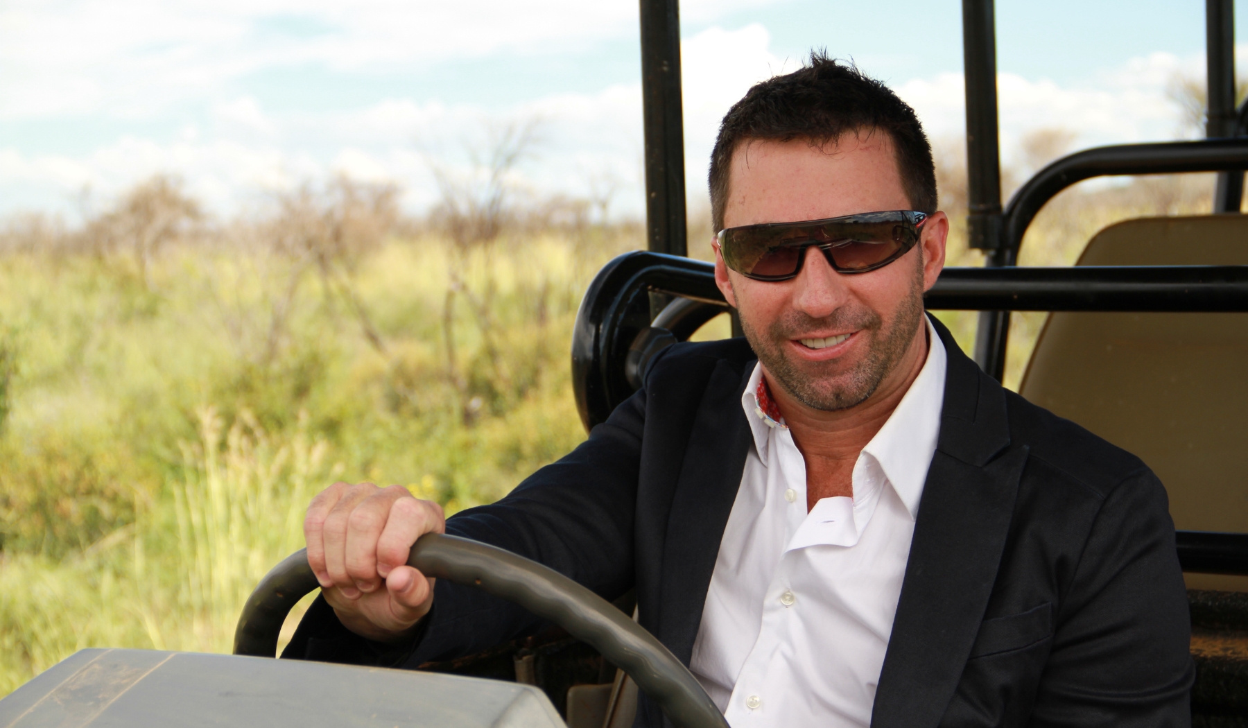 David Ryan sits behind the wheel of an open safari vehicle, smiling mid-drive, capturing a pivotal moment in the early story of Rhino Africa and Londolozi.
