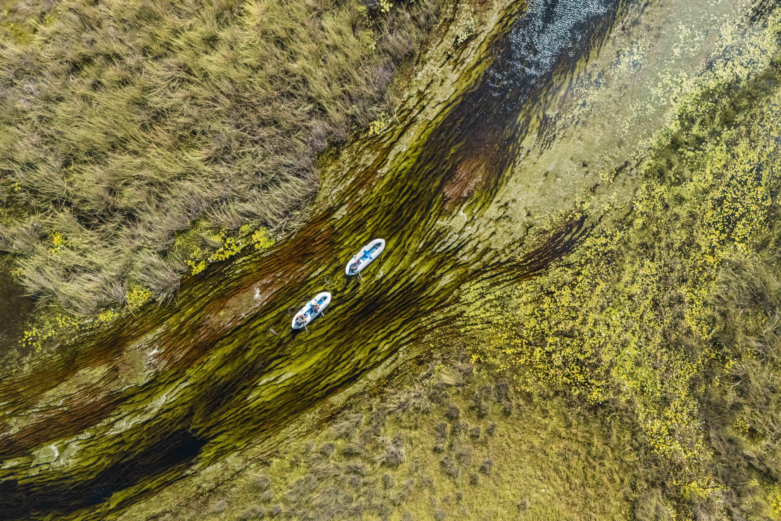 An aerial view shows two small boats drifting along a narrow, reed-lined water channel, exemplifying low-impact destinations for responsible travel.