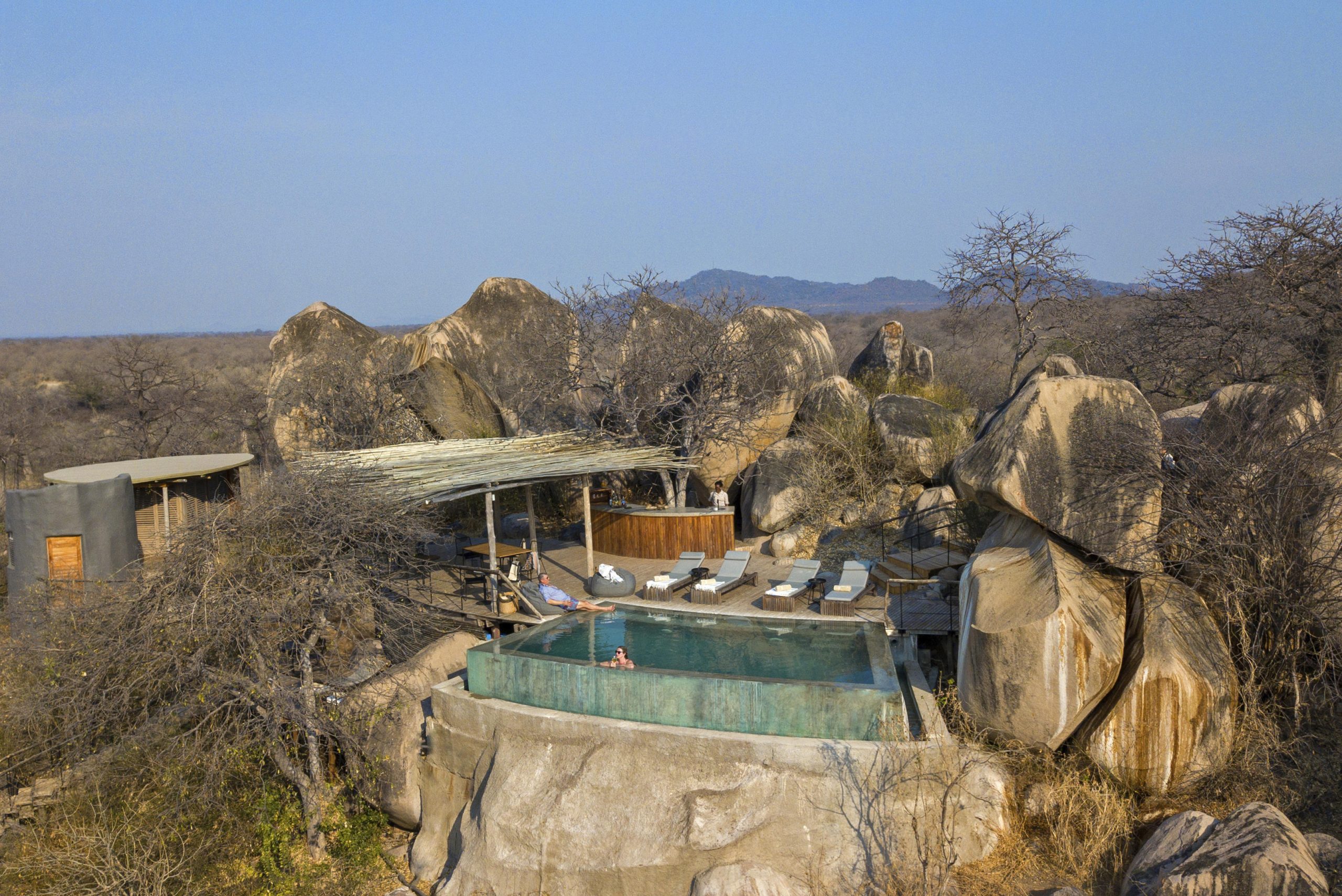 An infinity pool carved into granite boulders overlooks vast, dry Ruaha wilderness, capturing the dramatic setting of Luxury safari lodges in Tanzania.