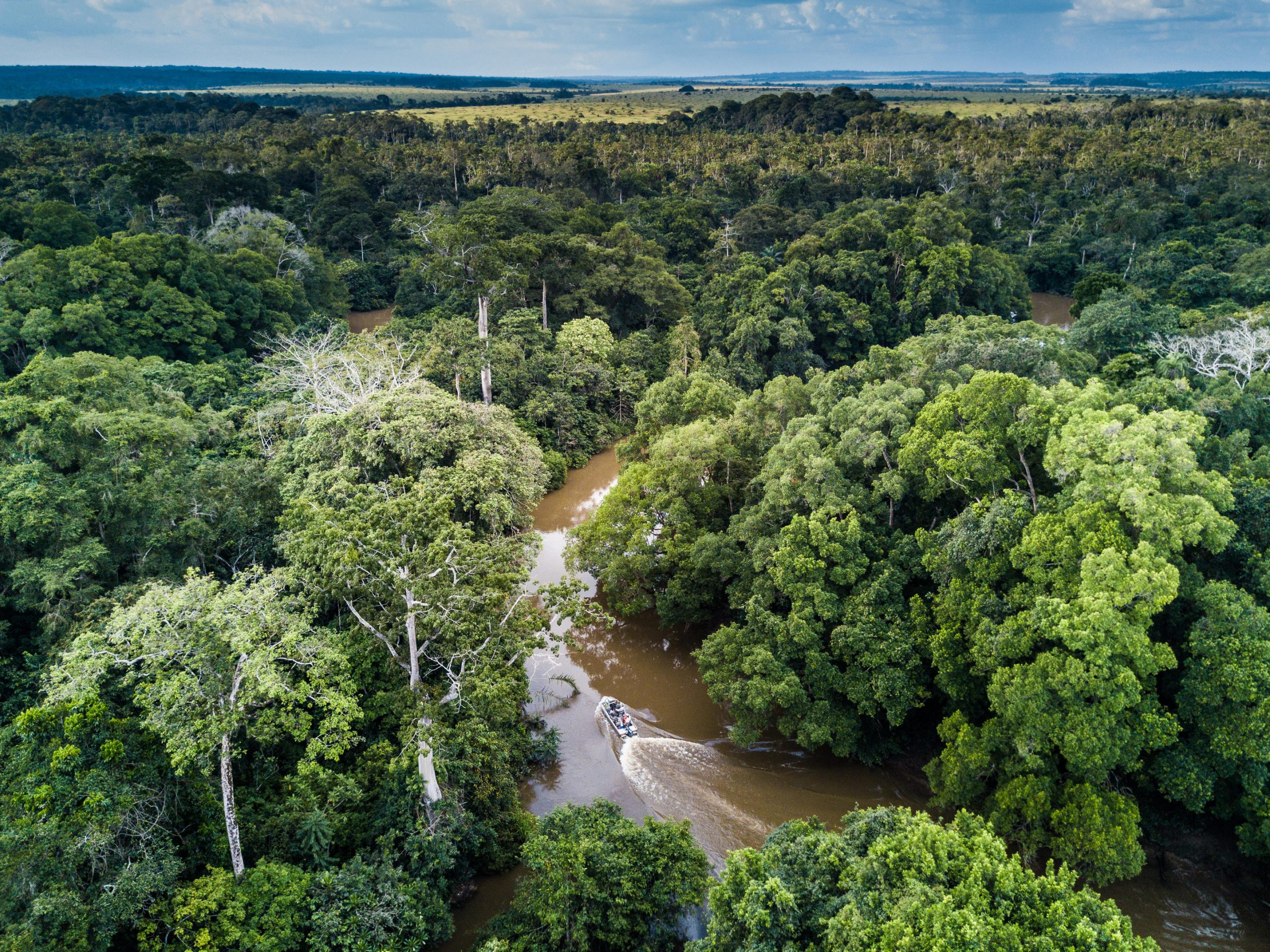 An aerial view shows a small boat travelling along a winding river through dense rainforest, capturing remote destinations for responsible travel.