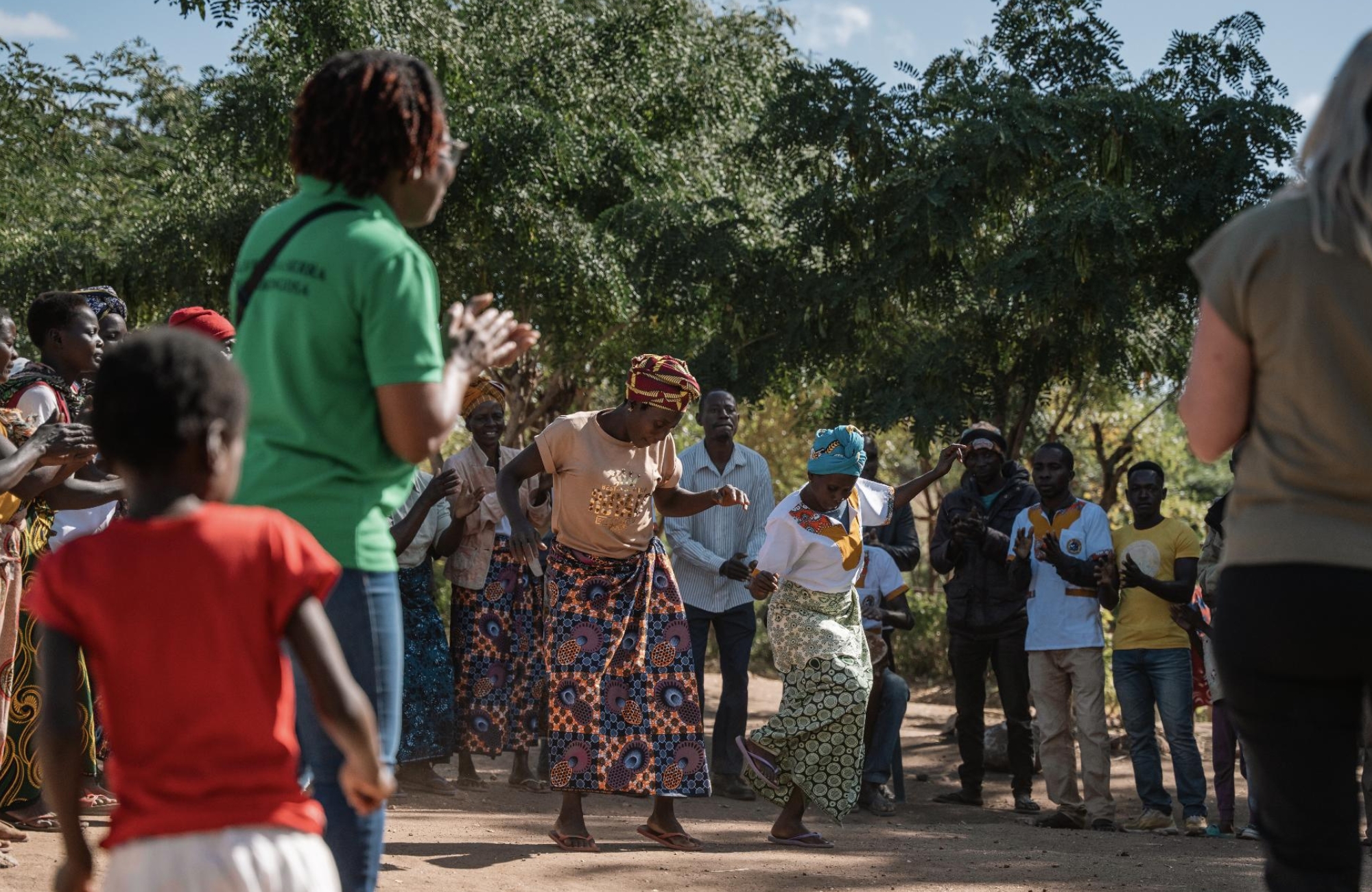impact-in-gorongosa-community-muzimu-lodge A group of local community members dance and clap together outdoors beneath trees, showing the impact in Gorongosa through shared participation, culture, and collective presence.