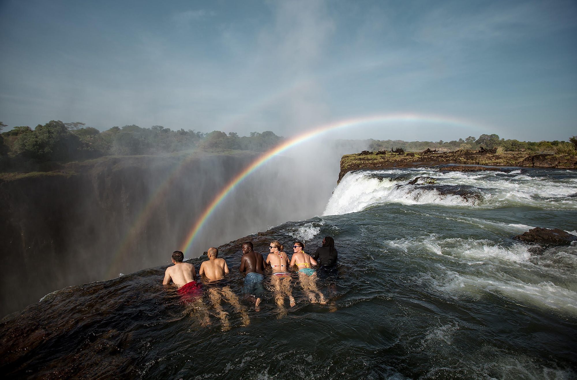 Five people swim in Devil's Pool on Victoria Falls, one of the most exciting activities to do on a Zimbabwe safari tour