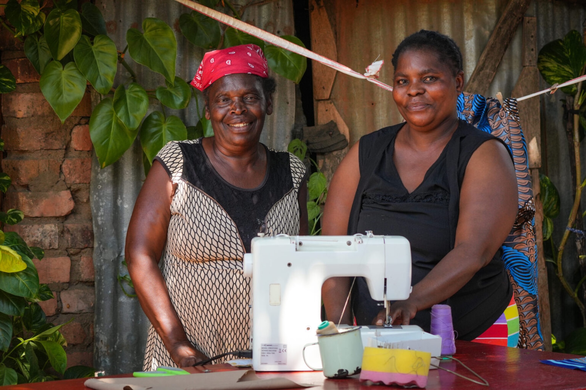Two women stand behind a sewing machine, crafting unique goods you can purchase on a Zimbabwe safari