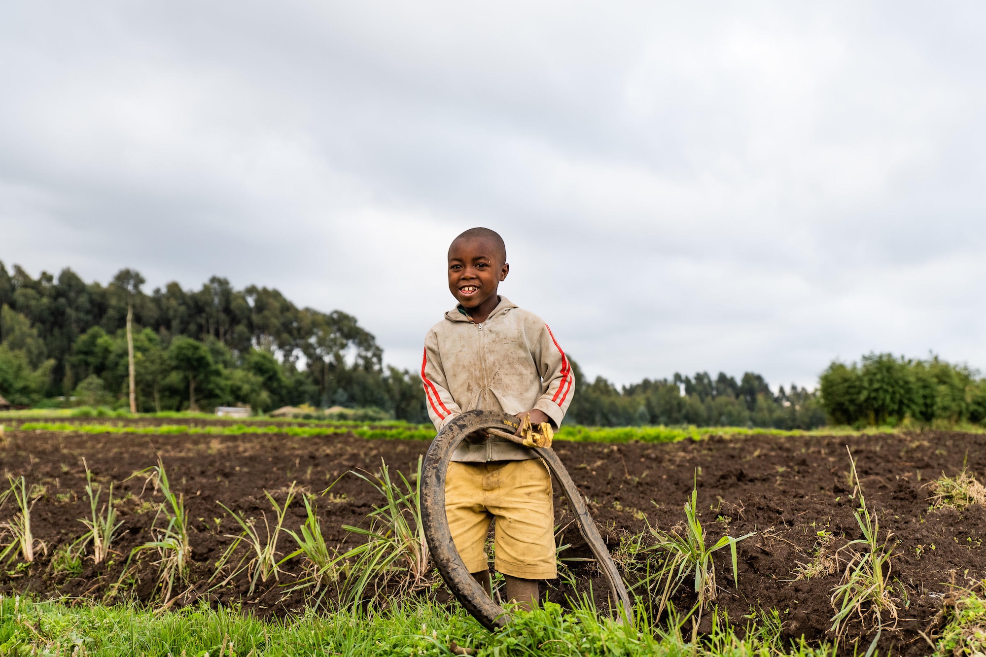 A child smiles standing in front of a farm in Rwanda