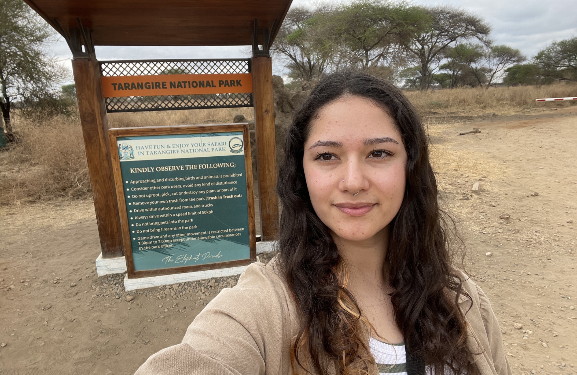 Rhino Africa Travel Expert Laura Hall stands in front of Tarangire National Park sign while on a Tanzania safari